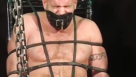 Bigg Pete roped down in chains with his mouth strapped shut