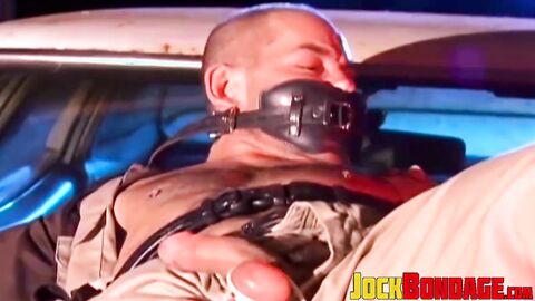 Submissive police officer tied up on the hood of a car